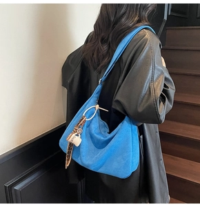 Blue velvet crossbody bag with coffee cup tassel charm shown on model in a sleek interior