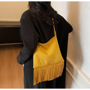Detalle de bolso bandolera de ante amarillo con flecos largos sobre una chaqueta negra