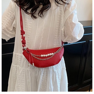 Détail du sac selle rouge tissé avec perles décoratives, chaînes et bandoulière nouée