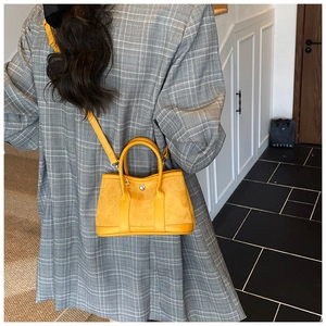 Detail of a bright yellow suede tote bag worn by a model in a modern indoor setting