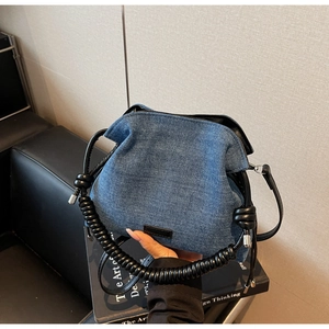Blue denim bucket bag featuring a thick black spiral handle and minimalist leather patch