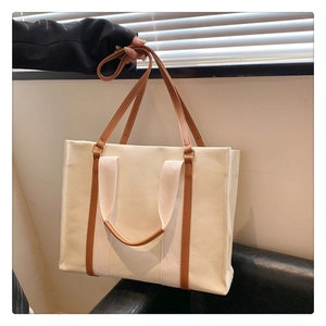 Detail of canvas tote bag showing cream fabric texture and brown leather strap handles