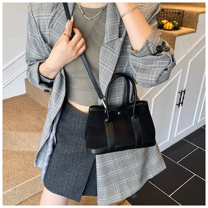 Chic black tote bag with dual handles and slender shoulder strap on female model