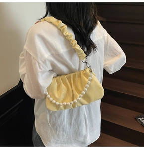Sac nuage plissé jaune pâle avec chaîne de perles porté par un mannequin sur escalier