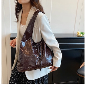 Detail of deep brown glossy leather tote bag with side drawstring worn with a white blazer
