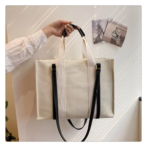 Close-up of cream canvas tote bag featuring black leather handles and long shoulder strap