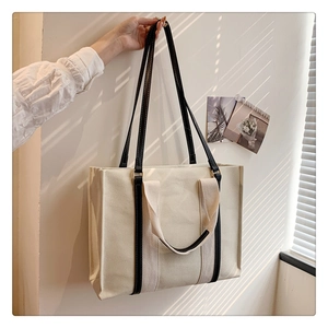 Minimalist canvas tote bag with black leather straps hanging against a sunny wall