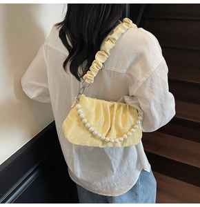 Détail du sac nuage jaune plissé avec chaîne de perles porté par un mannequin