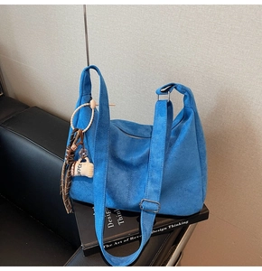 Detail of blue suede tote bag featuring coffee cup charm and smooth zipper on design books