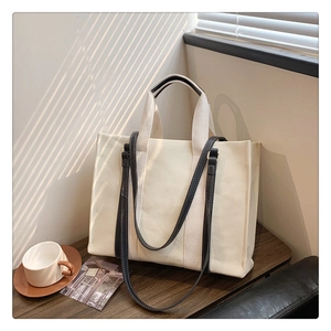 Detail of minimalist canvas tote bag showing black contrast handles on wooden table