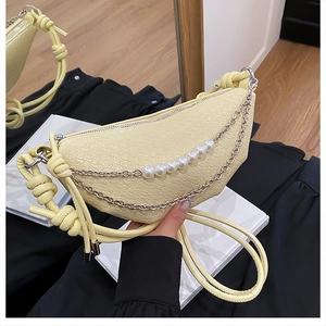 Détail du sac croissant crème avec texture crocodile, chaîne de perles et chaîne argentée