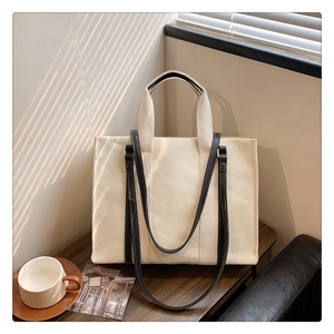 Detail of canvas tote bag with contrast leather trim and dual handles in soft sunlight
