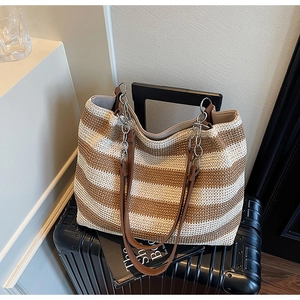Dettaglio di una borsa tote intrecciata a righe con tracolla in pelle e catena su una valigia