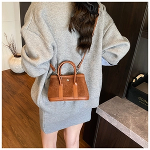Detail of a brown suede tote bag with leather trim and gold buckle in a casual setting
