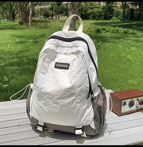 Outdoor backpack with white nylon pleats and gray base shown in a sunny park setting