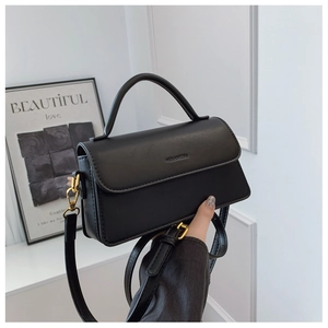 Detail of black leather shoulder bag showing gold metal hardware and matte finish texture