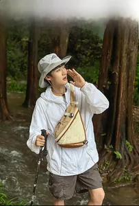 Outdoor crossbody bag shown with windbreaker and hiking poles in forest setting