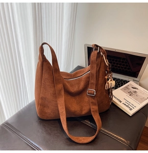 Detail of dark brown matte hobo bag with adjustable strap and plush charm on leather seat