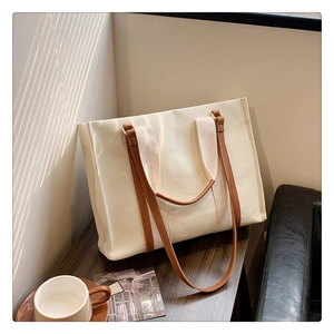 Detail of cream canvas tote bag with brown leather handles on dark wood tabletop