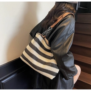 Dettaglio della borsa tote tessuta a righe con tracolla in pelle marrone e catena