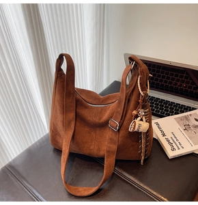 Detail view of brown suede tote bag with coffee cup pendant and adjustable strap on desk