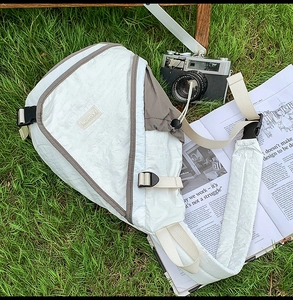 Flat lay of a white waterproof crossbody bag with FASHION label on green grass outdoors