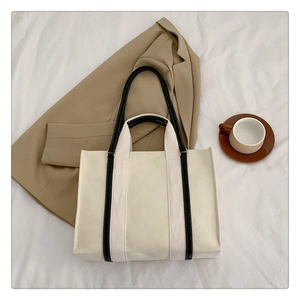 Detail of off-white canvas tote bag with black handles on a beige blazer background