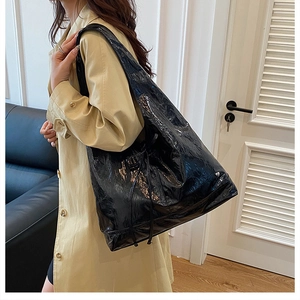 Detail of glossy black patent tote bag with silver heart charm on beige trench coat