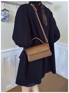 Brown leather vintage-style rectangular shoulder bag worn over a black outfit indoors