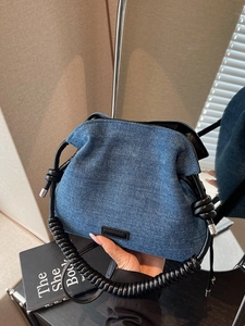 Chic blue denim dumpling bucket bag with unique black spiral top handle and knotted detail