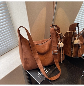 Detail of dark brown suede crescent bag with coffee-themed charm and tassel on wooden table