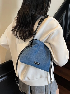Blue denim crossbody bucket bag with black spiral handle shown on model in casual style