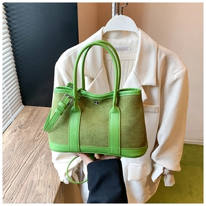 Detailed view of sage green tote bag with suede texture and metallic buckle on white blazer