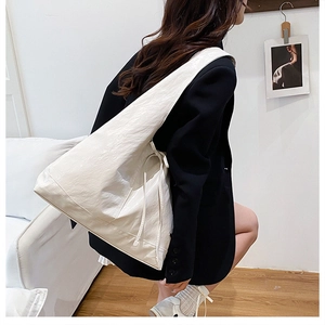 Detail of a large creamy white pleated leather tote bag worn by a model in a casual style