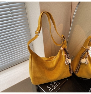 Detail of a yellow suede hobo bag with coffee cup charm and stylish fringe in soft light