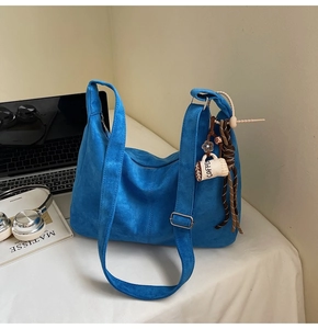 Detail of blue suede tote bag with coffee plush charm on desk with laptop and headphones