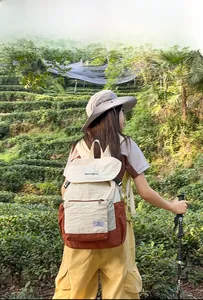 Outdoor canvas backpack in beige and brown color-blocking shown against a lush tea garden