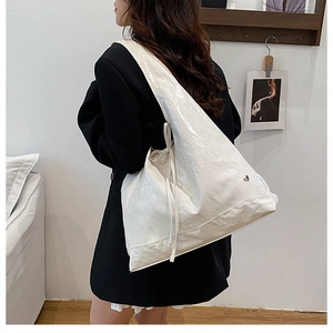 Detail of white glossy tote bag with bow accent and metal heart on model's shoulder