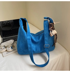 Detail of blue suede tote bag with coffee cup charm next to laptop and headphones
