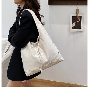 Detail of large white tote bag with side drawstring tassels and soft pleated texture