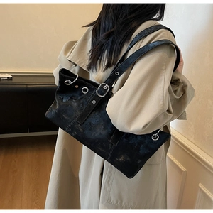 Detail view of retro black leather tote bag with silver eyelets on a khaki trench coat