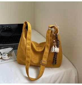 Detail of yellow suede tote bag with wide shoulder strap and coffee plush charm decoration
