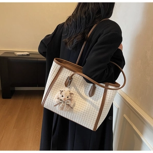 Rear view of a model wearing a white woven tote bag with brown leather trim and plush charm