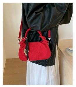 Detail of red suede bucket bag with heart pendant and woven tassel on black jacket