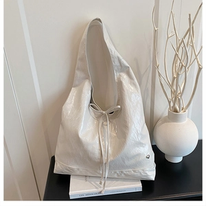 Detail of white crinkled patent leather tote bag with silver heart charm on a book