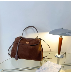 Detail der Vintage dunkelbraunen Wildleder-Tragetasche mit goldenem Drehverschluss auf Glastisch
