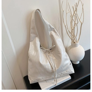 Detail of white glossy tote bag featuring a decorative bow and small metal heart logo