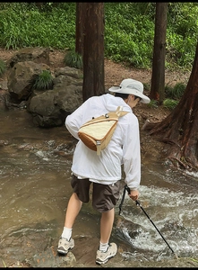 Outdoor crossbody bag shown on a model crossing a stream in a natural forest setting