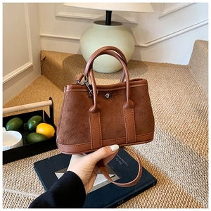 Detailed close-up of brown suede tote bag featuring smooth leather trim and metal clasp
