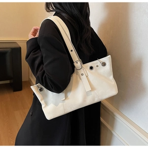 Detail view of white leather shoulder bag with silver eyelet grommets and adjustable strap